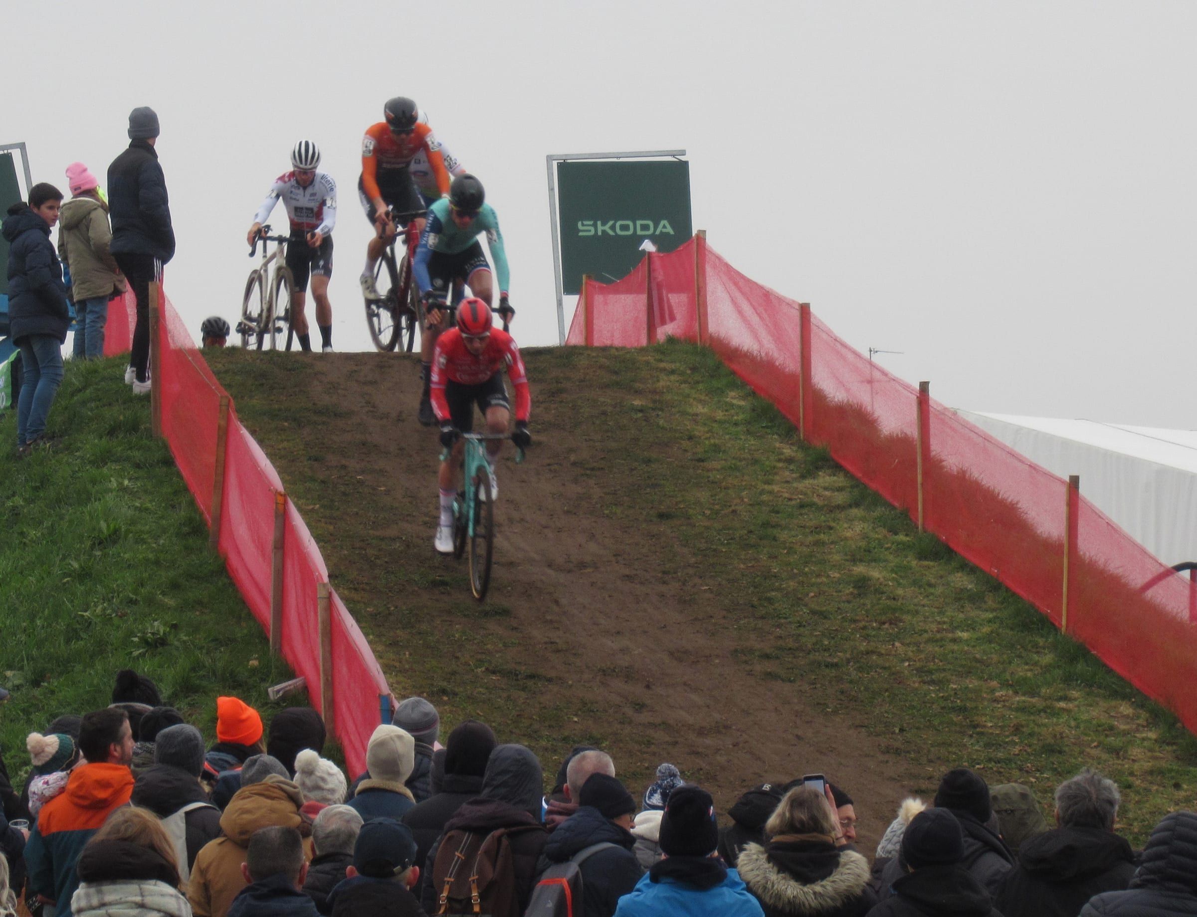 Quatre coureurs descendent une butte en herbe et en terre entre deux rubans rouges, au-dessus d'une foule en bonnets d'hiver.
