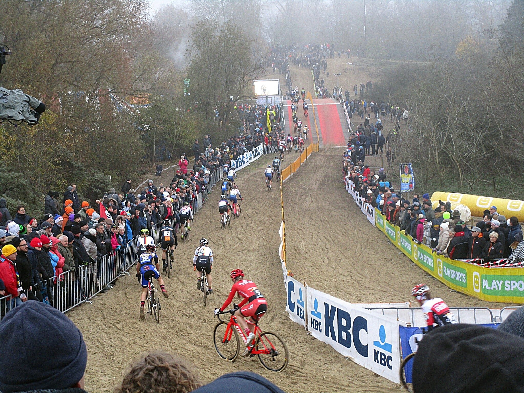 Vue plongeante sur la piste de sable des dunes de Coxyde, coureuses en file entre deux haies de spectateurs.