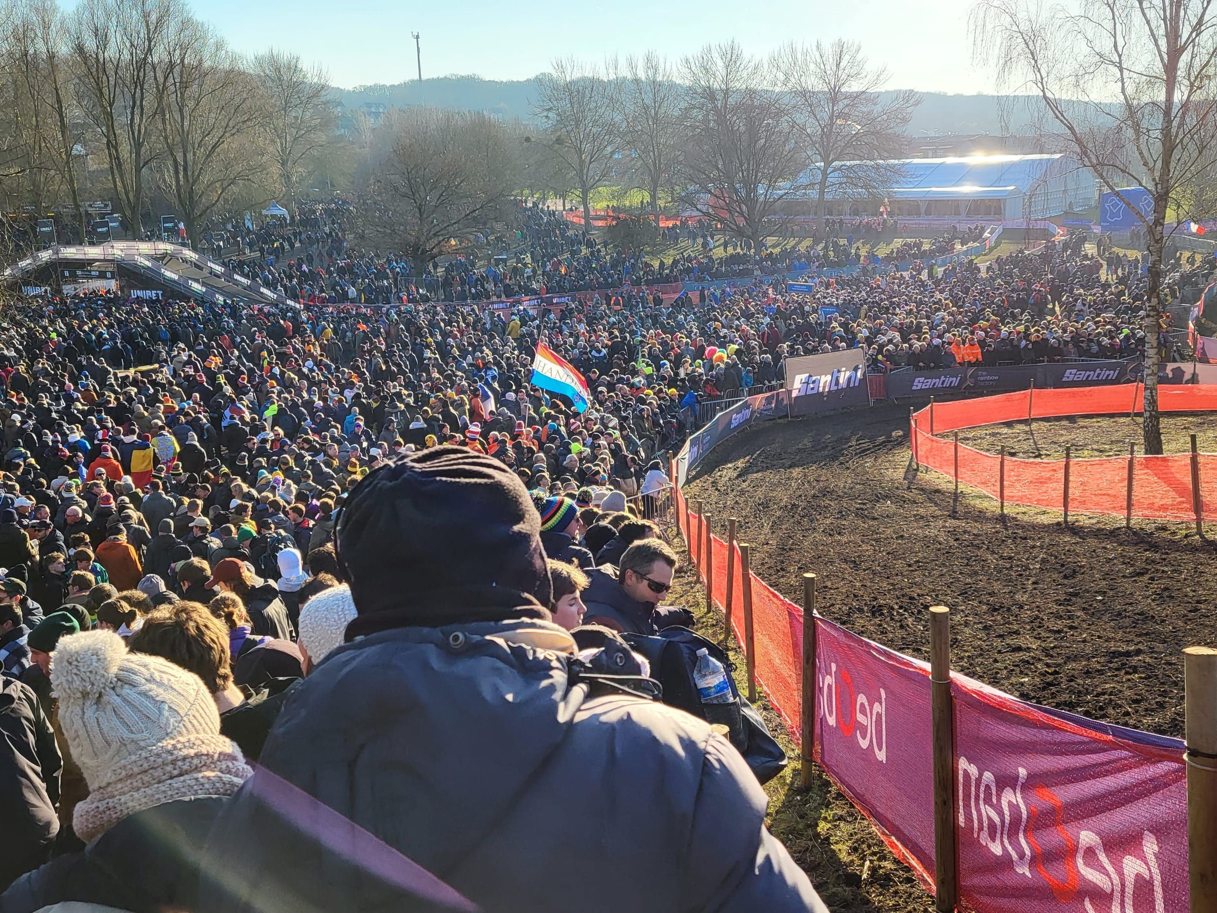 Une foule dense entoure le parcours boueux des Mondiaux, bordé de rubalise rouge, sous un soleil d'hiver.