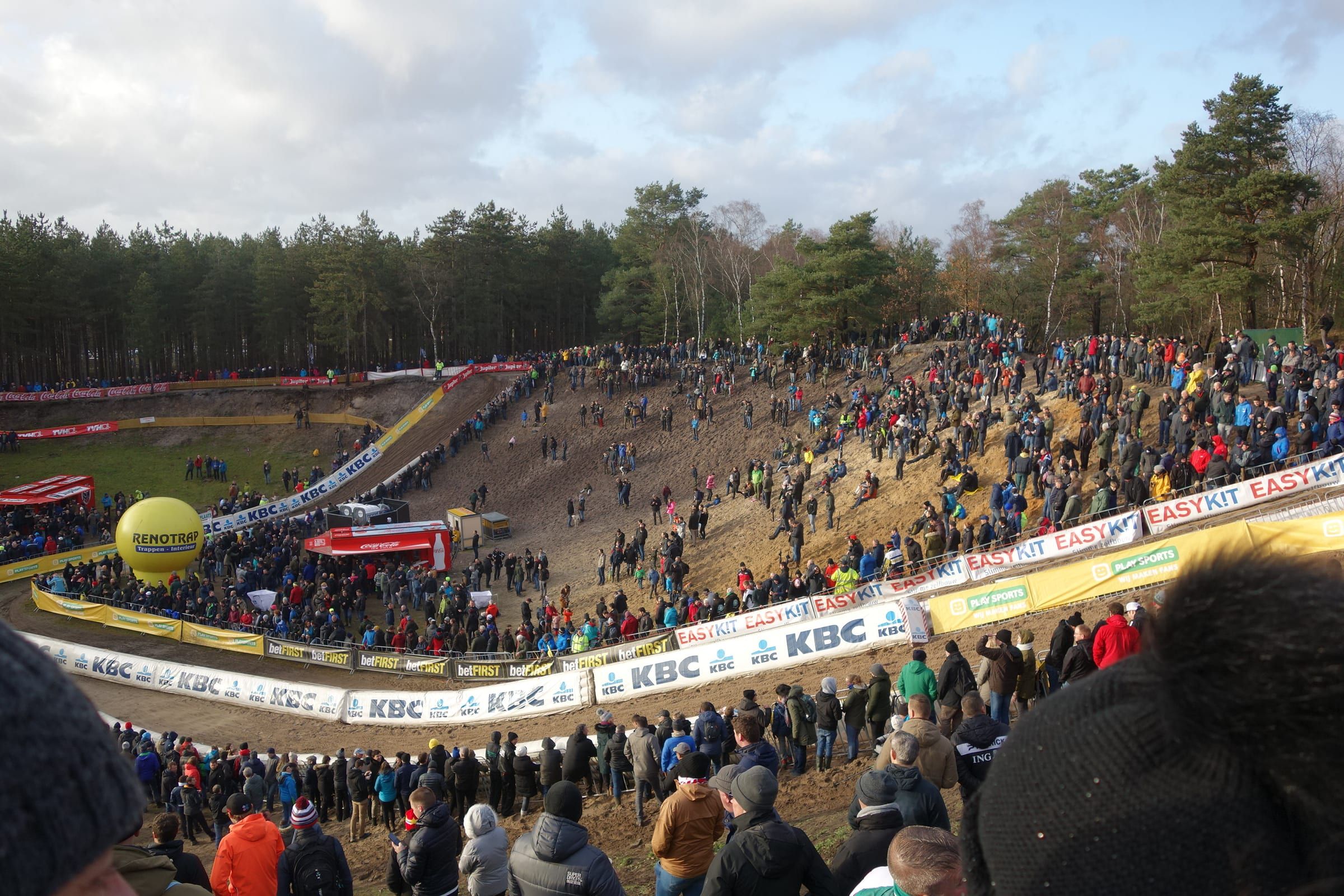 Panorama de la cuvette de sable de Zonhoven, ses pentes noires de monde et la forêt de pins autour.